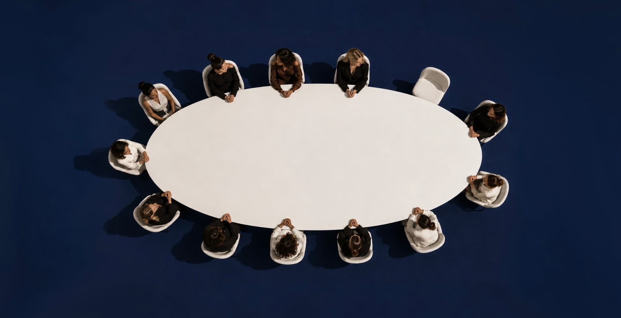 Twelve women seated around an oval table, seen from above