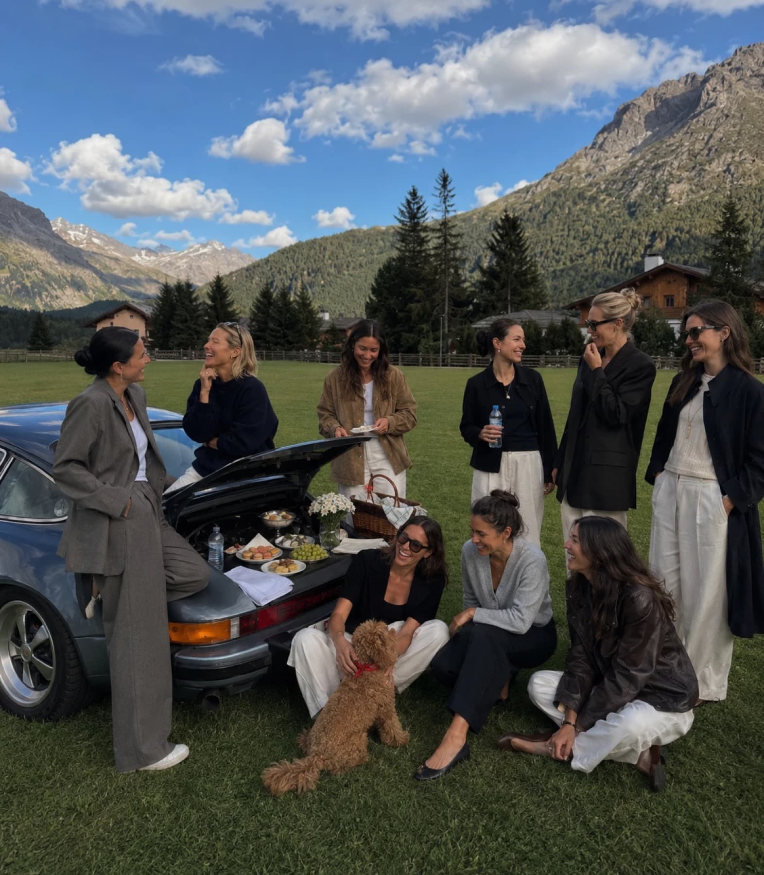 A group of women sharing a picnic by a car in a mountain valley